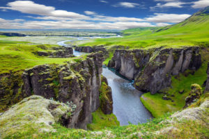 The striking canyon in Iceland. Bizarre shape of cliffs surround the stream with glacial water. The concept of active northern tourism